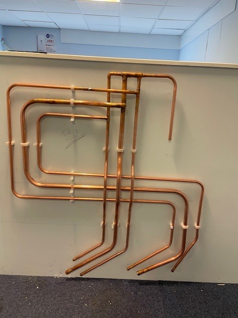 A copper pipe installation is attached to a beige coloured wall. Three pipes were installed parallel by Sam Mitchell at the SkillPLUMB Scottish Heat.